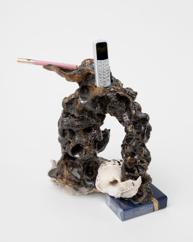 <i>Boudoir Phone tel,</i> 2025</br>
glazed ceramic, miniature cellular phone, shell from Haiti, </br>seashell, Chinese cigarettes 555, Russian cigarette</br> 27,5 x 25,5 x 10 cm / 10.8 x 10 x 4 in