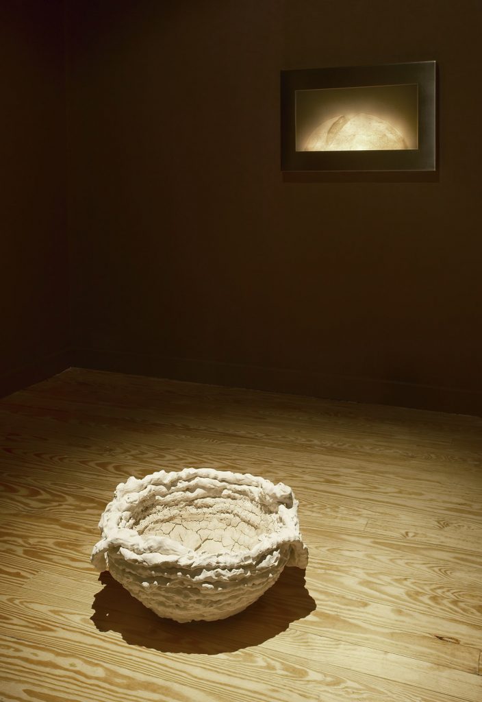 <I>inscape / becoming</I>, 2011
</br>
in foreground: white clay, sourdough crust coats interior
</br>
26 x 56 cm / 10.2 x 22 in 
</br>
on wall: corian lithophane, steel frame, light electronics
</br>
50 x 76 x 5 cm / 19.7 x 29.9 x 2 in>