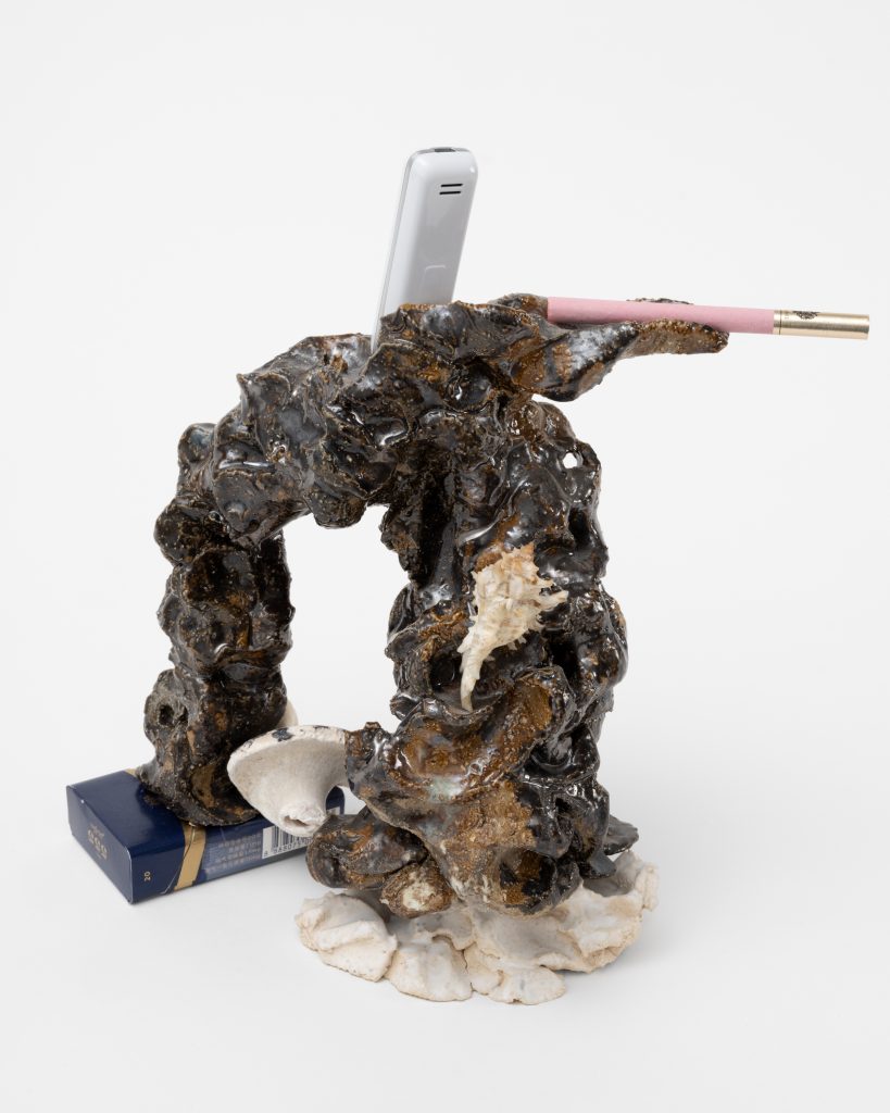 <i>Boudoir Phone tel,</i> 2025</br>
glazed ceramic, miniature cellular phone, shell from Haiti, </br>seashell, Chinese cigarettes 555, Russian cigarette</br> 27,5 x 25,5 x 10 cm / 10.8 x 10 x 4 in