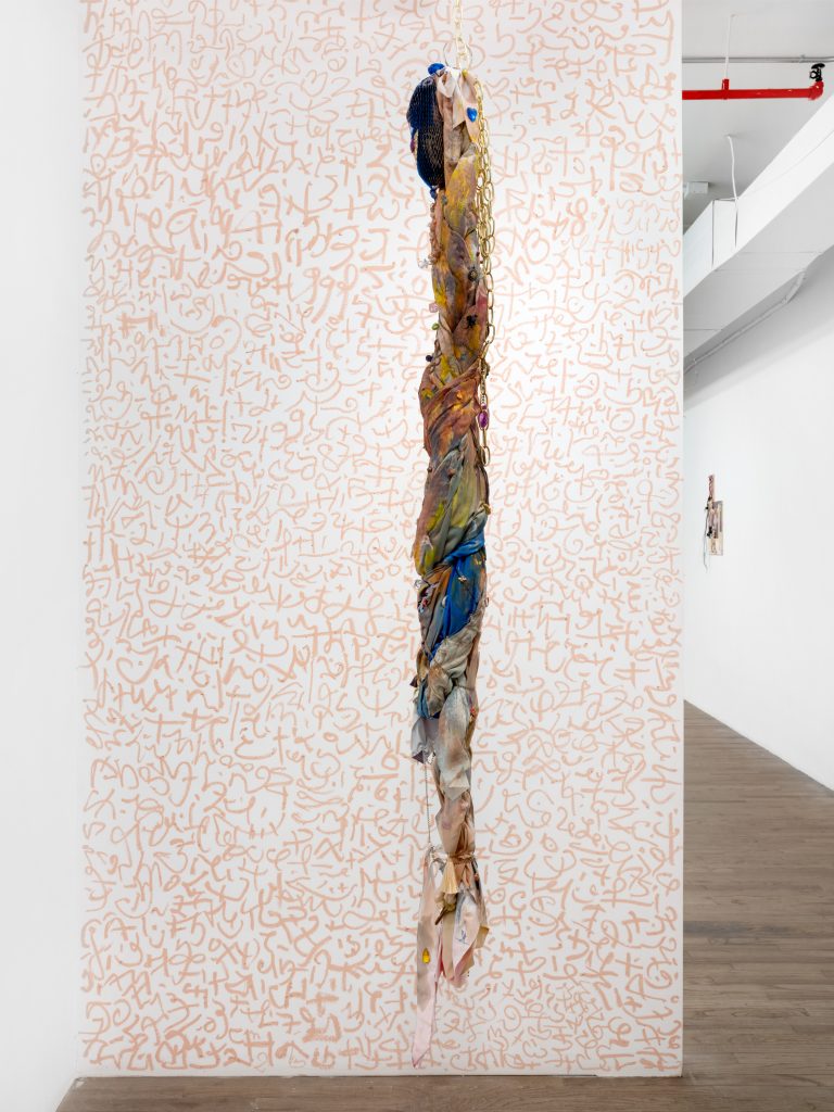 <i>Talisman por lo mojo,</i> 2025</br>
oil pastel site specific automatic talismanic writing </br>for protection and harmonization of energies, </br> feather, gems, key ring, brass chain, vibrational energy of purification and trust</br> 335,3 x 165,1 cm / 132 x 65 in