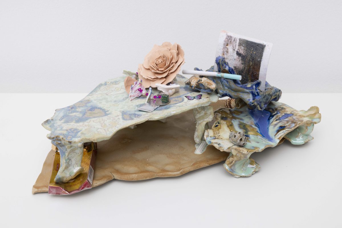 <i>Boudoir - Maybe close to the beach,</i> 2025</br>
glazed ceramic, film with the presence of salt, Chinese cigarette</br> shells, Chinese beads, a coin, a dice, matches, bubblegum paper, ceramic rose</br>15 x 43 x 22 cm / 5.9 x 16.9 x 8.6 in